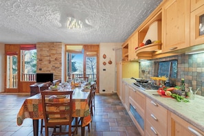 Cucina con mobili in legno, parete in pietra e zona pranzo con tavolo imbandito per quattro persone.
