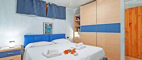 Un dormitorio con cama, mesita de noche, armario y ventana con cortinas.
