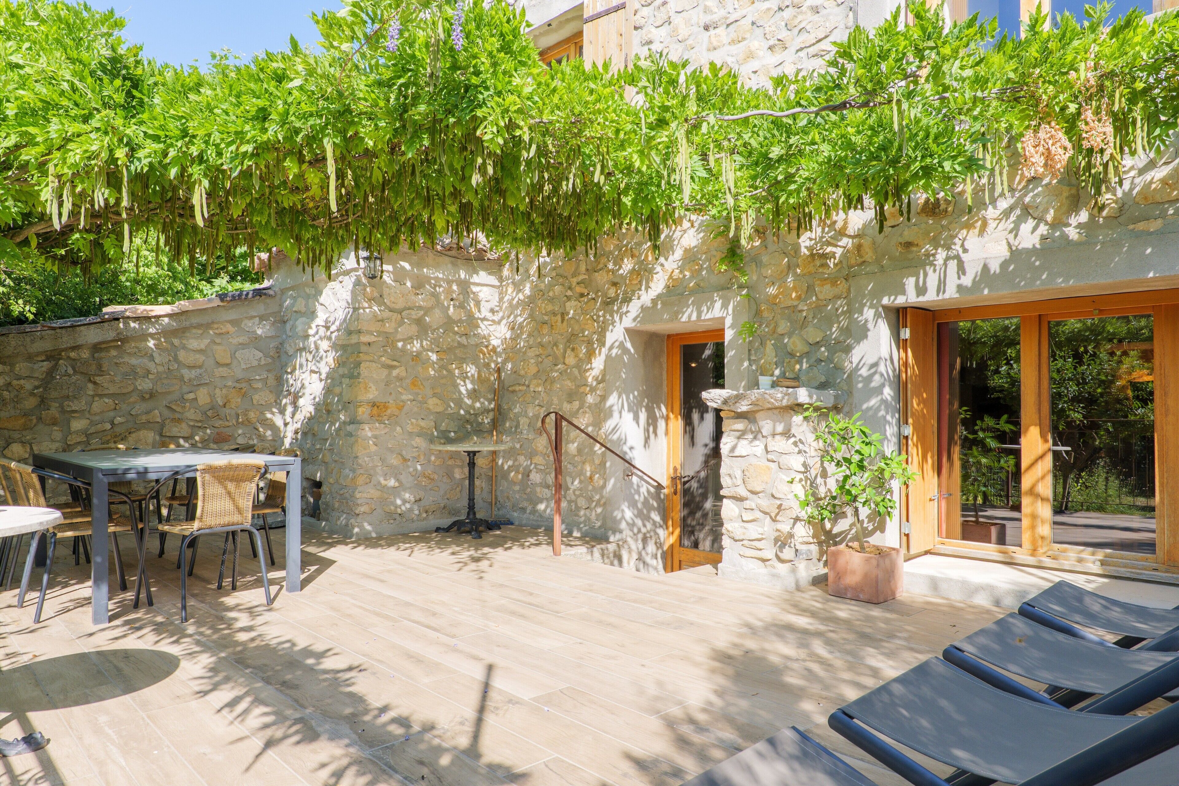 Un espacio al aire libre con paredes de piedra, una mesa y sillas, una planta en maceta y una puerta de madera.