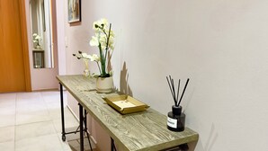 A hallway with a wooden table, a potted orchid, a bottle of perfume, and a reed diffuser. - 2 bedroom apartment - Rue Macé - 1mn Plage Croisette & Palais (Cannes)