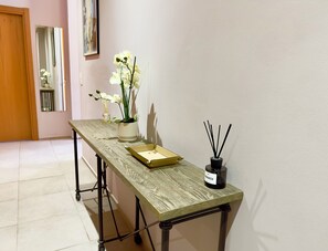 A hallway with a wooden table, a potted orchid, a bottle of perfume, and a reed diffuser. - 2 bedroom apartment - Rue Macé - 1mn Plage Croisette & Palais (Cannes)