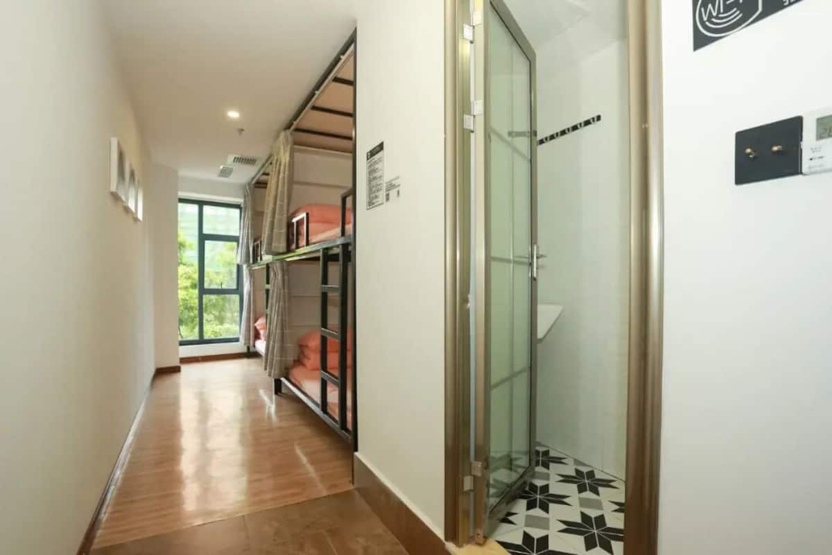 A hallway with a wooden floor, a glass door, and a bed with a pink blanket.