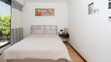 Un dormitorio con cama, mesita de noche, ventana con cortinas y una obra de arte en la pared.