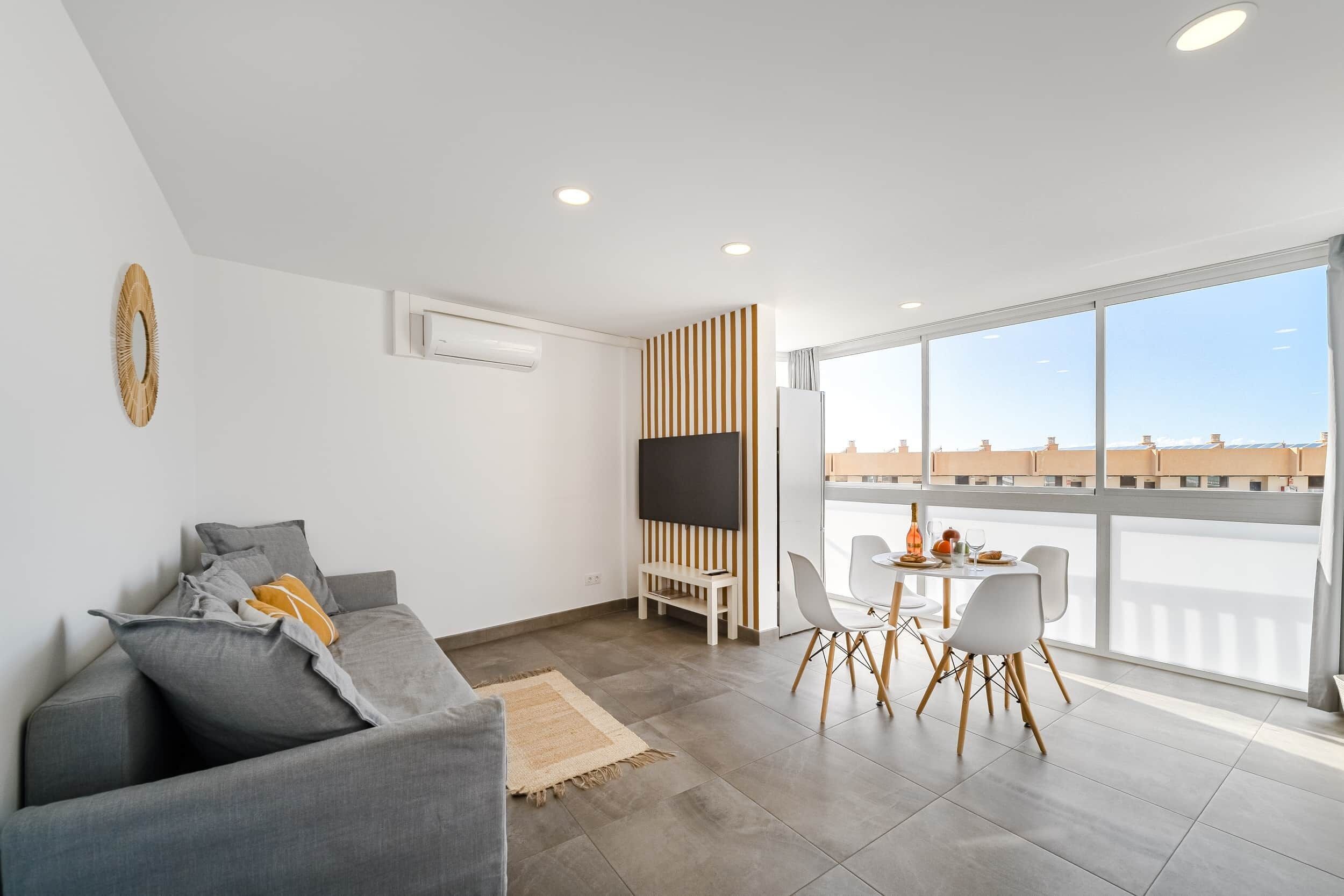A modern living room with a grey sofa, a TV, and a dining area with a table and chairs.