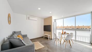 A modern living room with a grey sofa, a TV, and a dining area with a table and chairs.