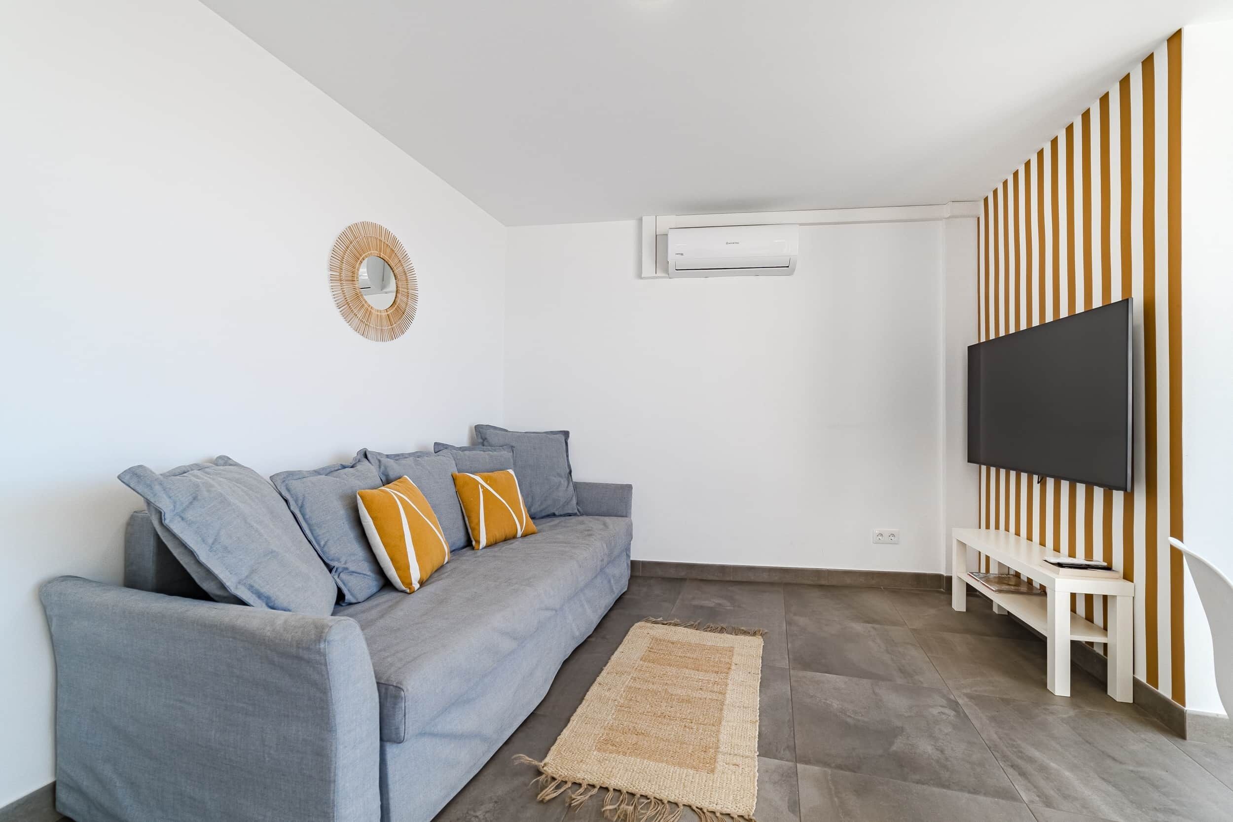 A modern living room with a grey sofa, a flat-screen TV, a woven rug, and a striped wall.