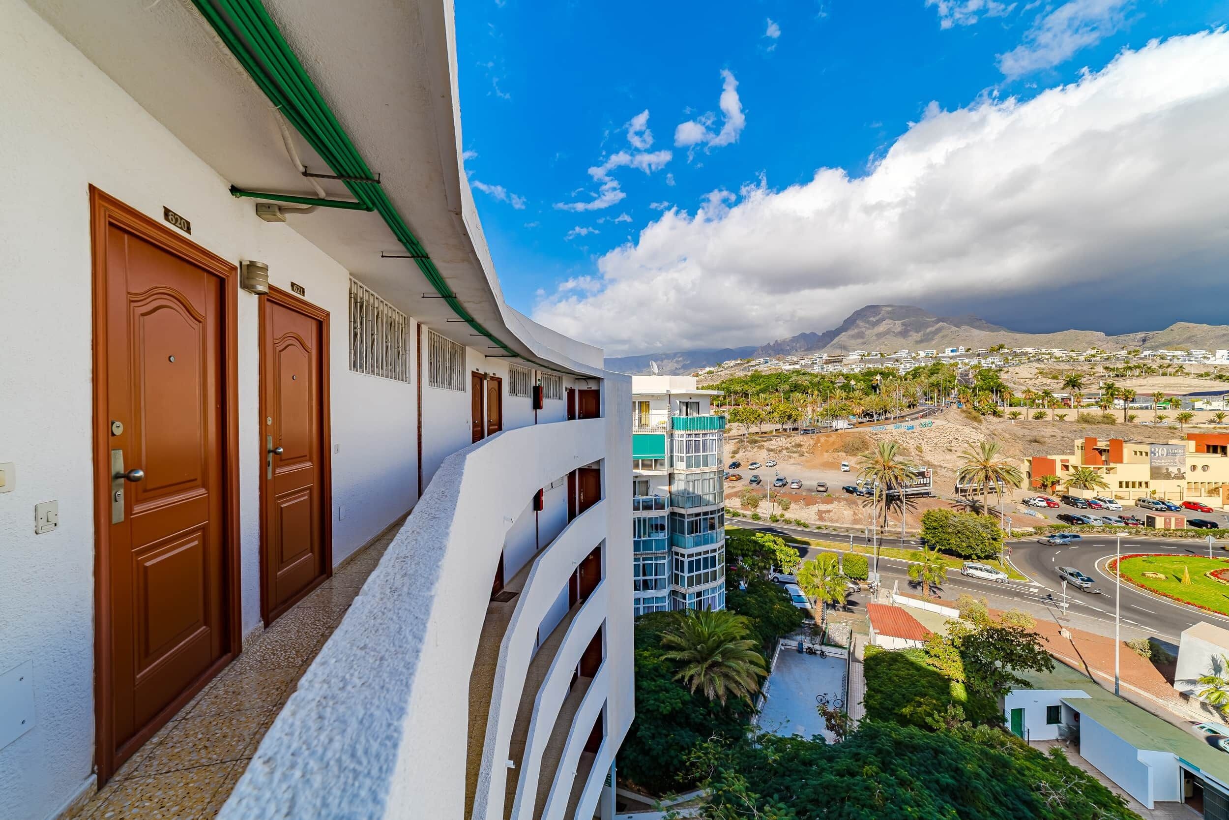 A hotel with a curved balcony overlooking a cityscape, including a road with cars and palm trees.