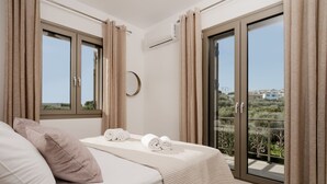 A bedroom with a bed, two pillows, a bedside table, and a view of a balcony with curtains. - Casa Lydia - 5 Bedrooms, Private Pool & Sea Views (Zakynthos)