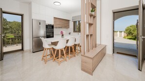 A modern kitchen with a central island, white cabinetry, and a view of the outdoors. - Casa Lydia - 5 Bedrooms, Private Pool & Sea Views (Zakynthos)