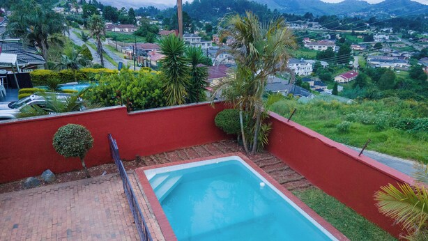 A rectangular swimming pool with a red border, surrounded by a brick patio and a red wall. - Perfect 8-bedroom lodge in Mbabane for your group getaway (Mbabane)