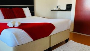 A neatly made bed with white and red bedding, a headboard, and a small bedside table with a microwave. - Perfect 8-bedroom lodge in Mbabane for your group getaway (Mbabane)