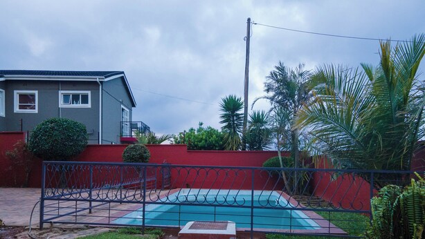 A residential backyard with a swimming pool, a red wall, and a metal fence. - Perfect 8-bedroom lodge in Mbabane for your group getaway (Mbabane)