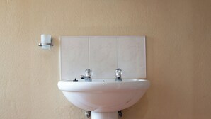 A bathroom with a white pedestal sink, a mirror above it, and a toilet paper holder on the wall. - Perfect 8-bedroom lodge in Mbabane for your group getaway (Mbabane)