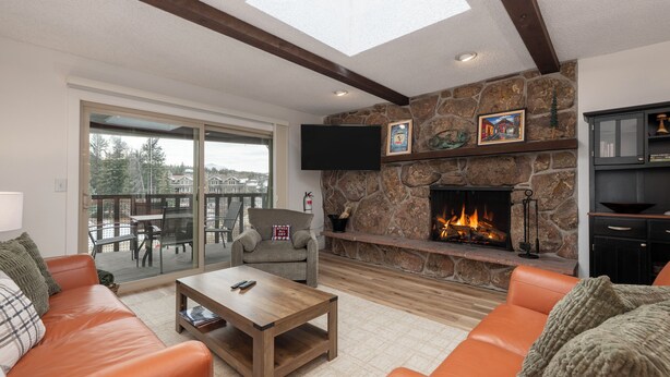 A living room with a stone fireplace, leather sofas, a coffee table, and a TV mounted on the wall. - Hi Country Haus Unit 2312 New, renovated 2 bedroom, private deck extra amenities (Winter Park)