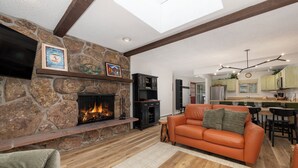 A living room with a stone fireplace, an orange sofa, and a wooden coffee table. - Hi Country Haus Unit 2312 New, renovated 2 bedroom, private deck extra amenities (Winter Park)