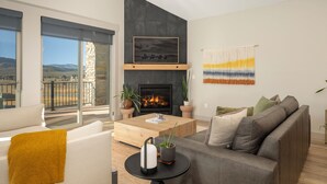 Ein modernes Wohnzimmer mit Kamin, einer Couch, einem Couchtisch und Blick ins Freie.