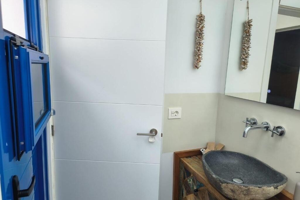 A bathroom with a white door, a sink with a stone basin, and a mirror above the sink.