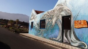 A building with a mural of a wave, a spa sign, and a clear sky. - Apartamentos Puntagrande - Unique experience in front of the Atlantic Ocean in El Hierro (Frontera)