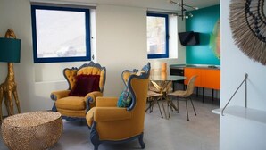 A modern living room with a yellow armchair, a round woven ottoman, and a dining area with a table and chairs. - Apartamentos Puntagrande - Unique experience in front of the Atlantic Ocean in El Hierro (Frontera)
