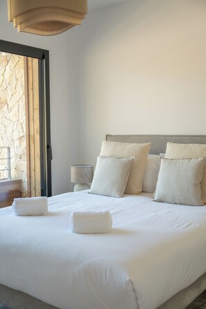 A neatly made bed with pillows and a folded towel, a bedside lamp, and a stone wall.