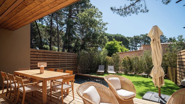Eine Holzterrasse mit Tisch, Stühlen, einem kleinen Pool und Korbmöbeln.