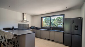 Eine moderne Küche mit Kochinsel, Barhocker, einem großen Fenster und einem schwarzen Kühlschrank.