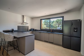 A modern kitchen with a central island, bar stools, a large window, and a black refrigerator.