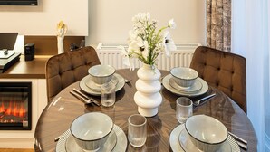 A dining area with a round table set for six, a clock on the wall, and a fireplace in the background. - ApartSanok - Apartament Widokowy 27-49 (Sanok)