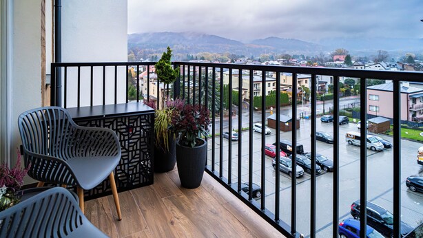 A balcony with two chairs, a small table, and two potted plants. - ApartSanok - Apartament Widokowy 27-49 (Sanok)