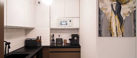 A modern kitchen with white cabinets, a black countertop, and a coffee machine.