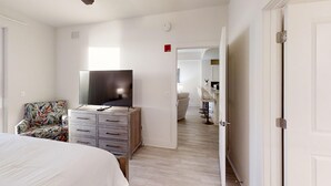 Ett sovrum med en säng, en tv placerad på en byrå i trä, en stol och en dörr som leder till ett badrum.