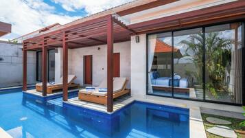 Un espace moderne aménagé au bord de la piscine, doté d’un coin salon couvert, offrant une vue dégagée sur la piscine et comprenant une grande fenêtre donnant sur celle-ci.