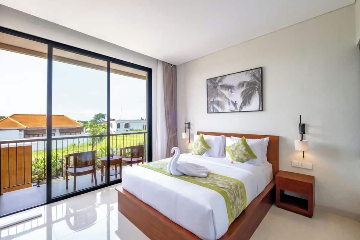 Ein modernes Hotelzimmer mit einem großen Balkon, einem Bett mit weißer Bettwäsche und grünen Kissen, einem Holz-Kopfteil und einem gerahmten Kunstwerk an der Wand.