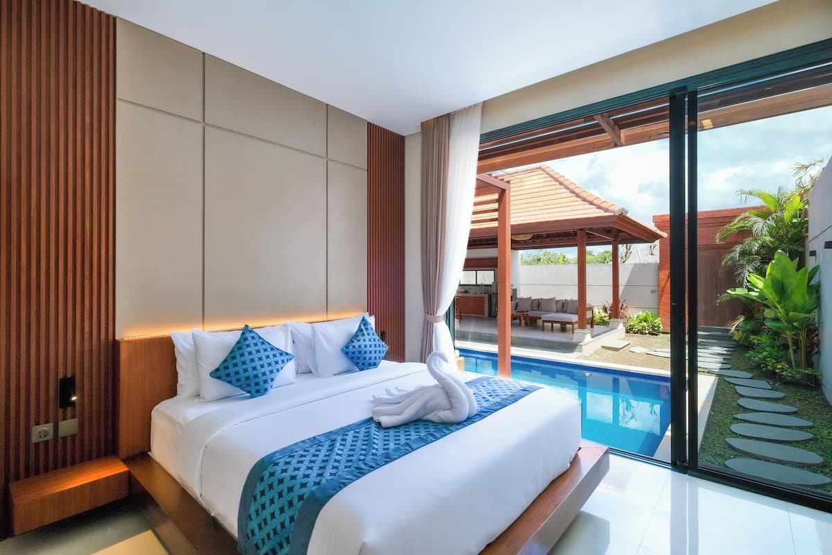 Ein modernes Hotelzimmer mit einem großen Bett, Blick auf einen Swimmingpool und einer Terrasse mit Gartenmöbeln.