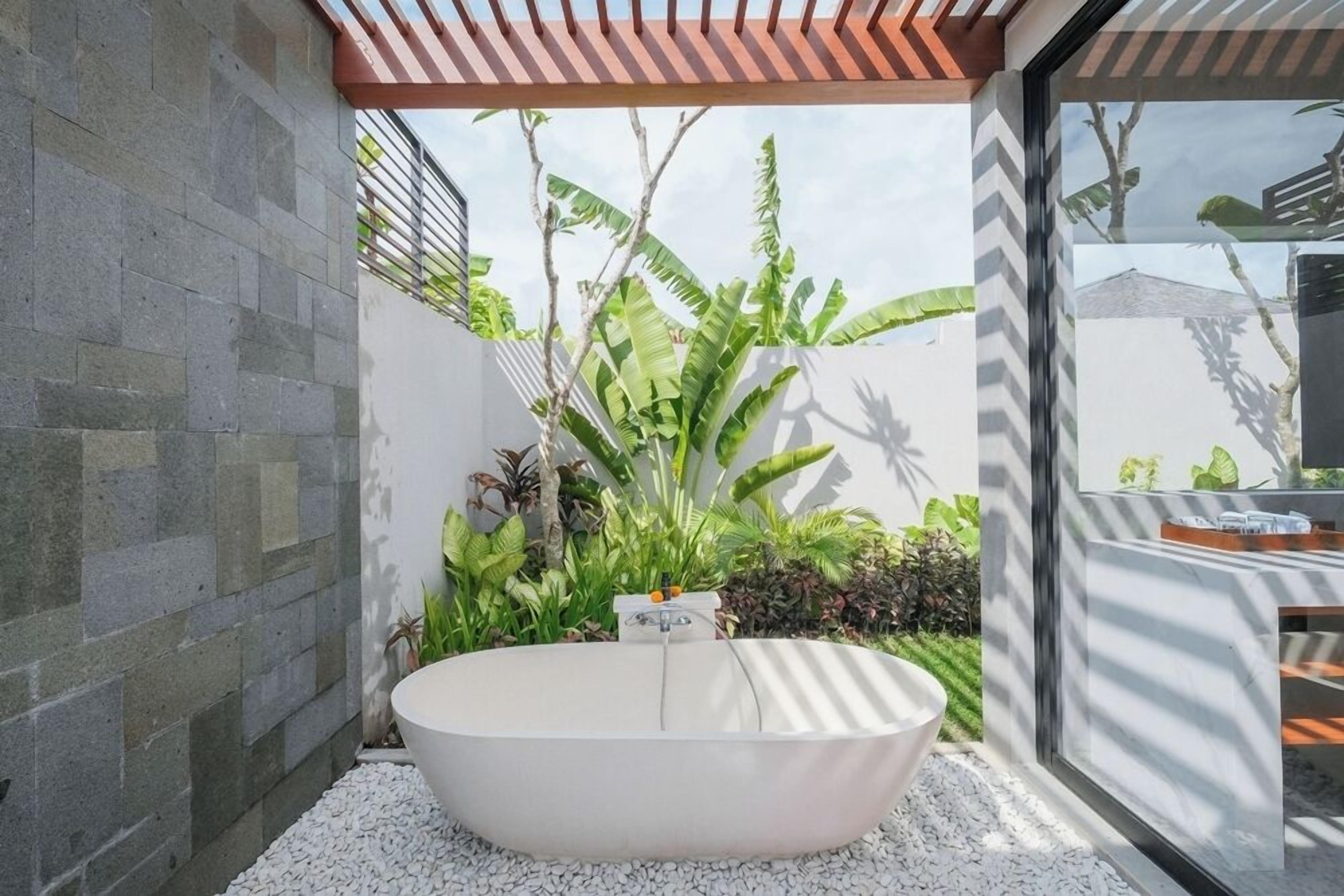 Une salle de bain moderne avec une baignoire sur pieds, entourée de galets blancs et d’une végétation luxuriante.