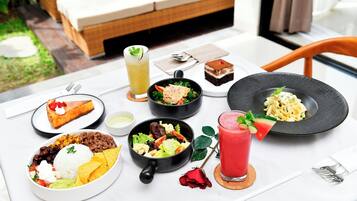 A table set with various dishes including rice, beans, salad, and desserts, with a rose and a drink on the table.