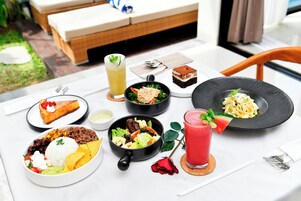 A table set with various dishes including rice, beans, salad, and desserts, with a rose and a drink on the table.