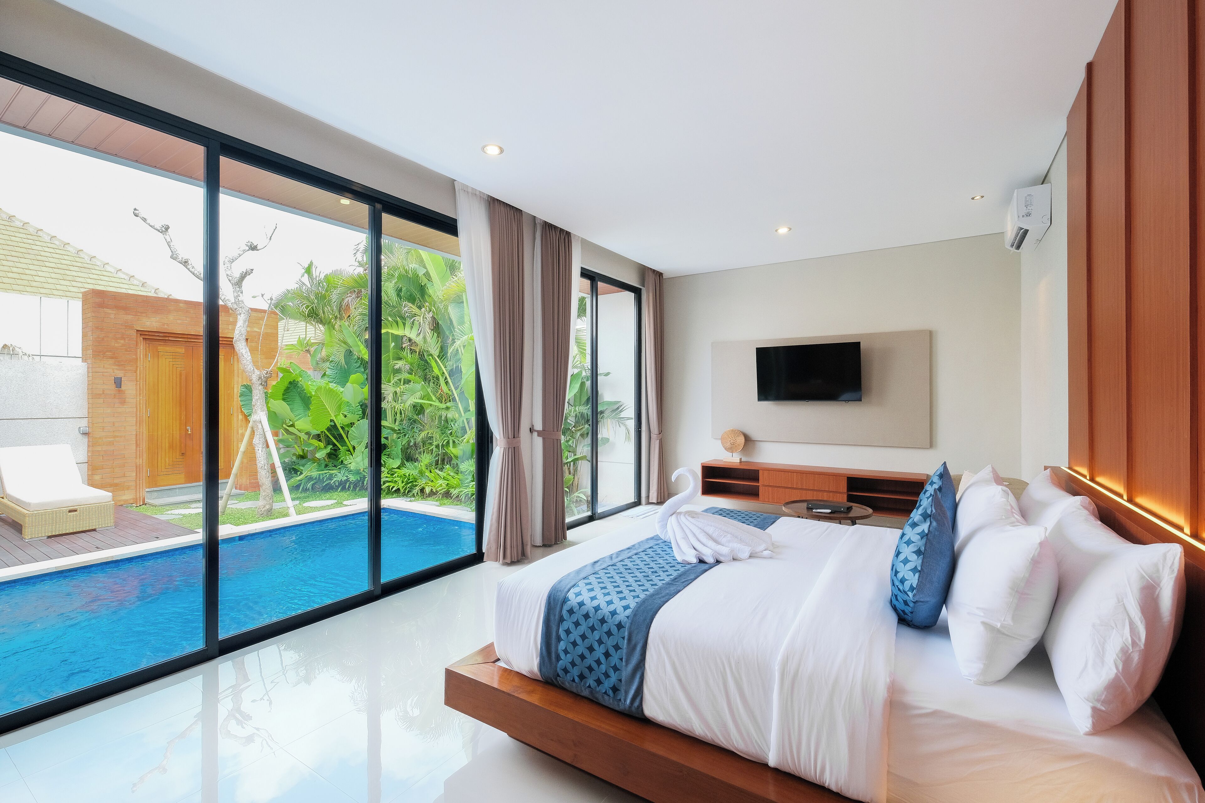A modern hotel room with a large bed, a flat-screen TV, and a view of a swimming pool.