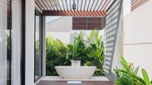 A modern outdoor area with a large white planter, surrounded by lush green plants and a wooden deck. - Three Brothers Villas and Suite Munggu (Munggu)