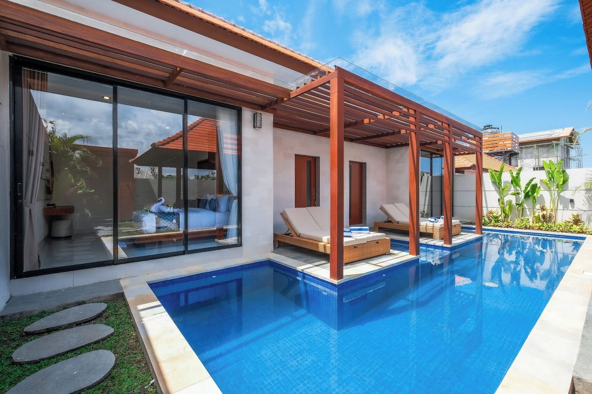 Ein moderner Poolbereich mit einem klaren, blauen Pool, einer Holz-Pergola und Liegestühlen.