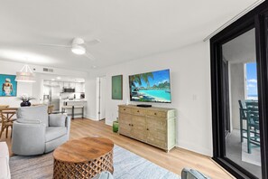 A modern living room with a grey sofa, wooden coffee table, and a television displaying a tropical beach scene. - New Listing! Stunning Renovated Beachfront 2BR/2BA • Sleeps 8• 6th-Floor (Orange Beach)