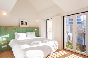 A bedroom with a bed, a green headboard, a window with a view, and a balcony. - Chic Duplex with Rooftop Terrace in City Centre (Lisbon)