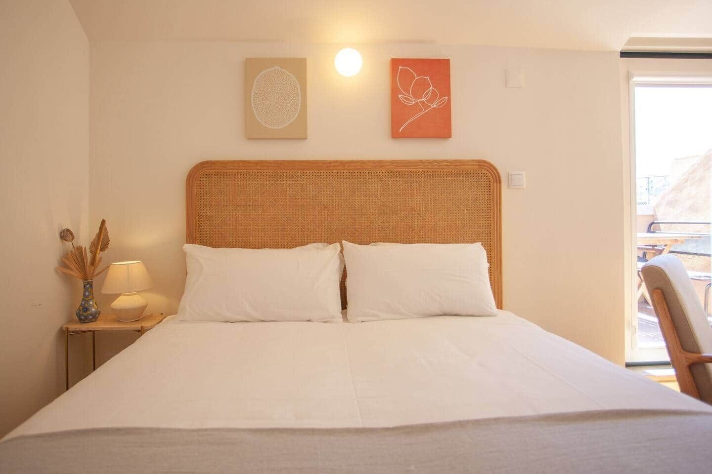A neatly made bed with a woven headboard, a bedside table with a lamp, and two wall art pieces.