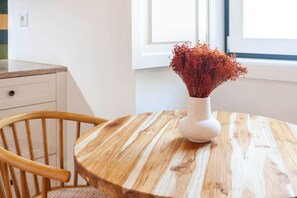 Ein runder Holztisch mit einer weißen Vase, gefüllt mit roten Blumen, ein Holzstuhl und ein Fenster im Hintergrund.