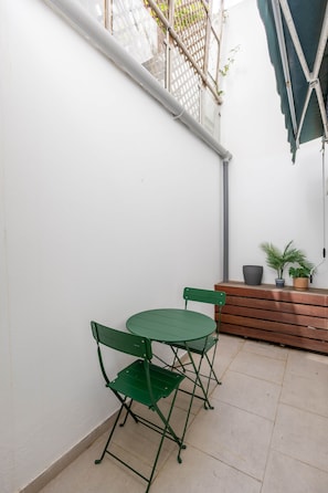 A small patio area with a green metal table and chairs, a wooden bench, and potted plants. - Stylish Oasis in Trendy Historic Centre Quarter (Lisbon)