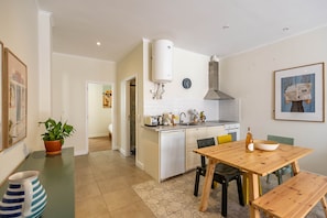 A modern kitchen with white cabinets, a stainless steel range hood, and a dining area with a wooden table and chairs. - Stylish Oasis in Trendy Historic Centre Quarter (Lisbon)