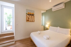 A hotel room with a bed, a window with a plant, a painting on the wall, and an air conditioning unit. - Stylish Oasis in Trendy Historic Centre Quarter (Lisbon)