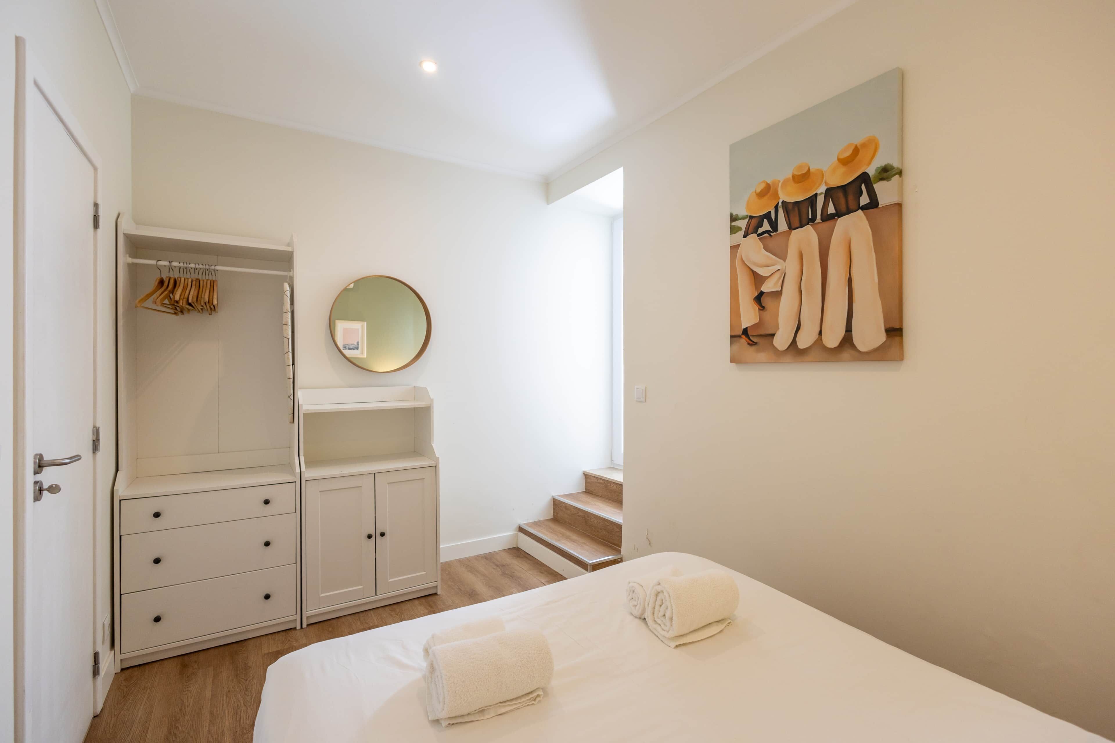 A bedroom with a bed, a wardrobe, a mirror, and a painting on the wall.