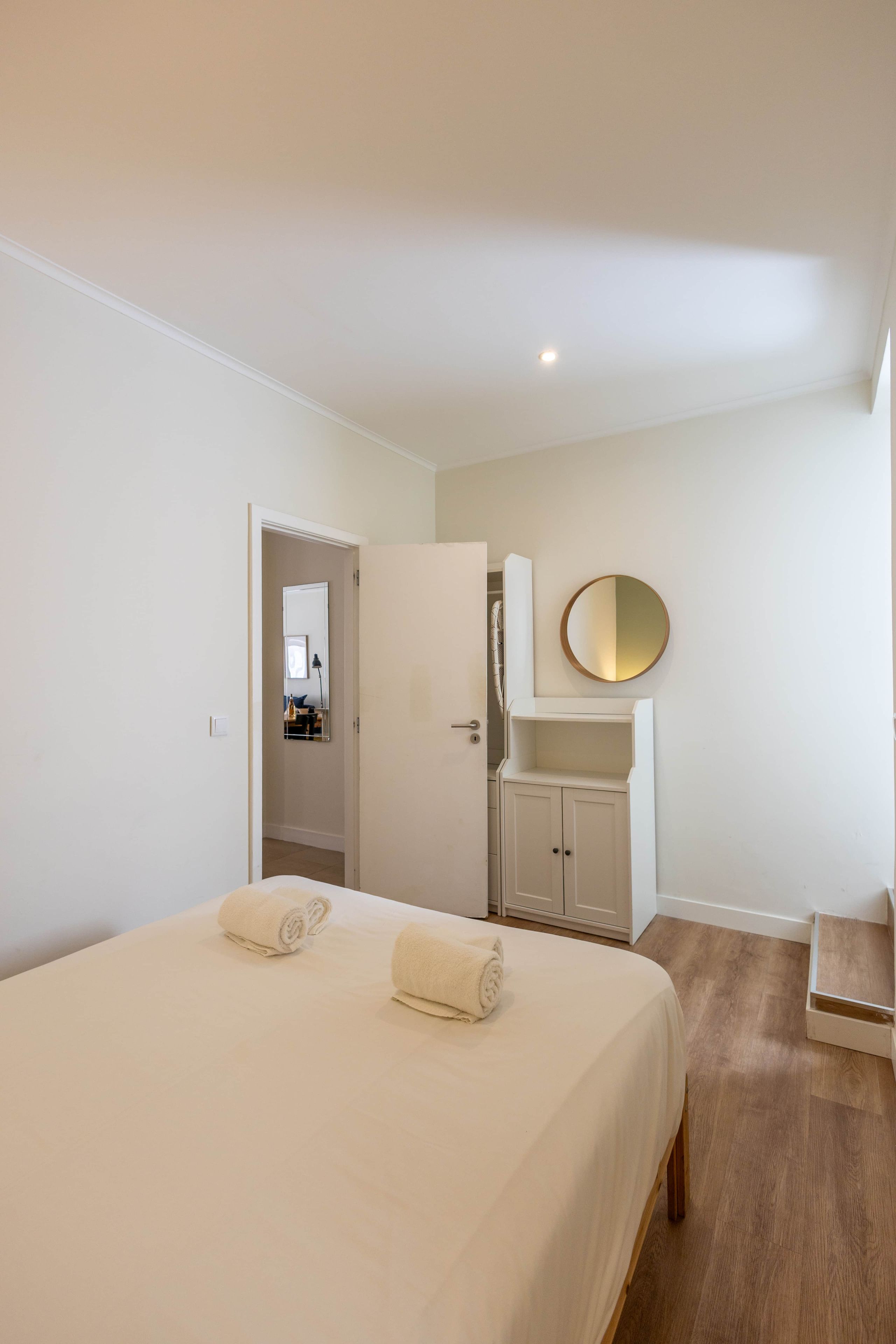 A hotel room with a bed, a wardrobe, a mirror, and a small seating area.
