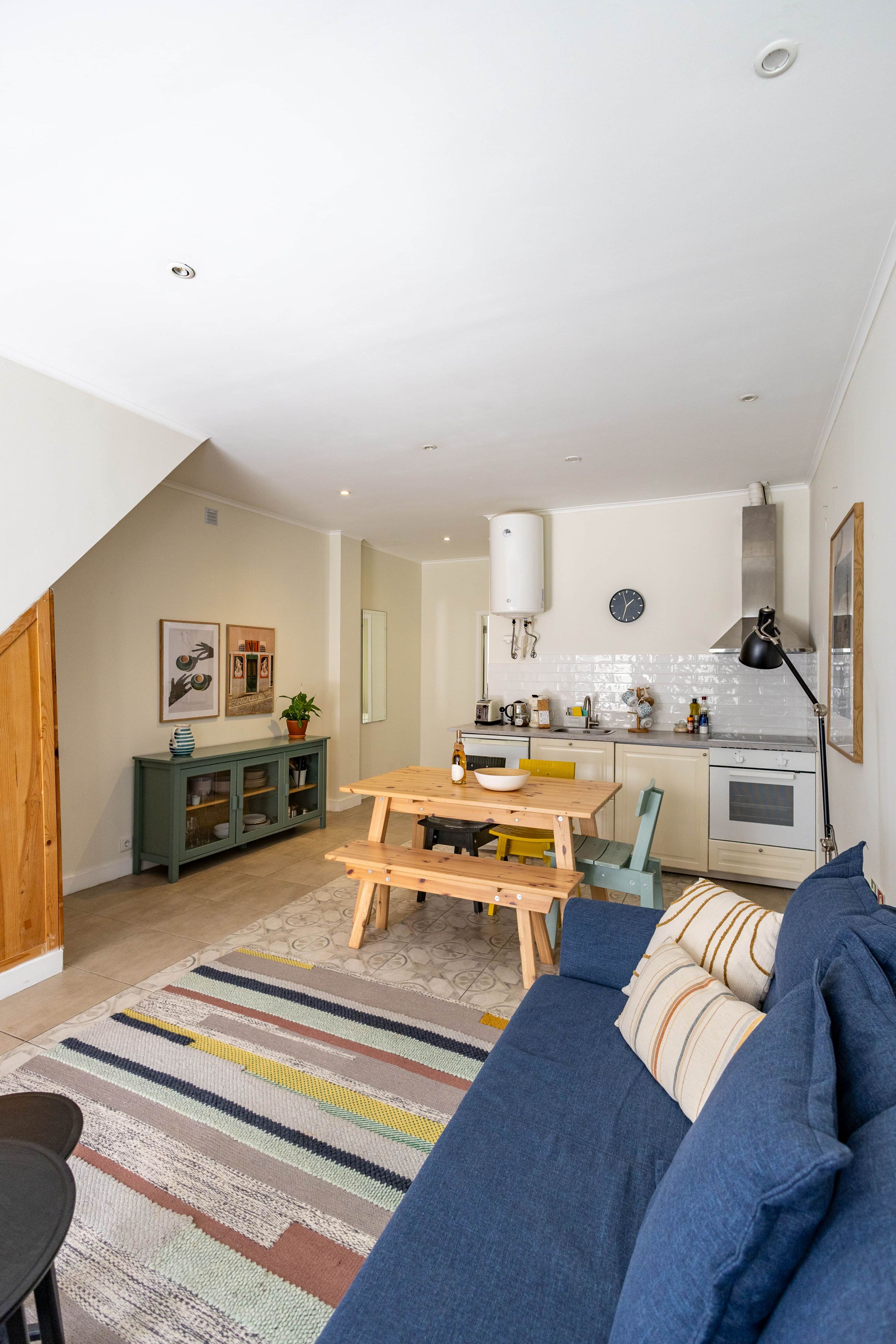 A modern living room with a sofa, a dining table, and a kitchen area with a stove and sink.
